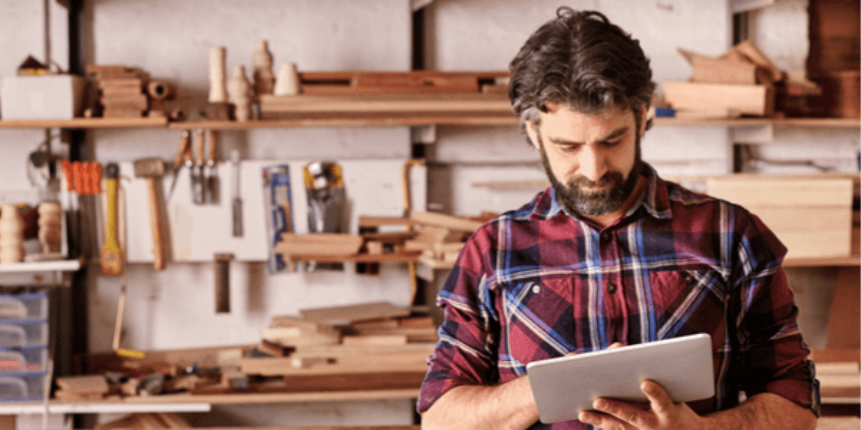 A tradeperson in a workshop using a tablet to create a quote via their job management software